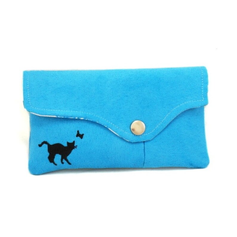 May include: A small, bright blue fabric clutch with a flap closure and a single button. The clutch has a black embroidered silhouette of a cat chasing a butterfly.