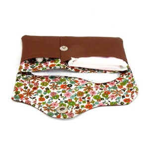 May include: A brown fabric pouch with a floral print lining. The pouch is open and has a white sanitary pad and tampons inside.