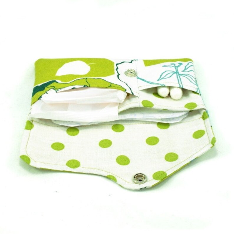 May include: A green and white fabric pouch with a polka dot pattern and a floral design. The pouch has a snap closure and is open to reveal a white sanitary pad and cotton swabs.