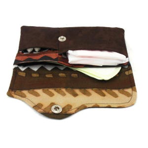 May include: A brown and tan patterned fabric pouch with a flap closure and snap button. The pouch is open and contains a white sanitary pad and a white tissue.