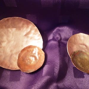 May include: Three copper bowls of varying sizes, with a hammered texture. The largest bowl is the lightest in colour, while the smallest bowl is the darkest.