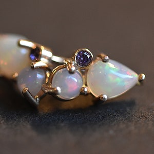 Puede incluir: Un anillo de oro con un grupo de tres &oacute;palos blancos con destellos iridiscentes y dos peque&ntilde;as piedras preciosas redondas de color violeta intenso. Las piedras est&aacute;n engastadas con garras, creando un dise&ntilde;o sobre una banda de oro pulido.