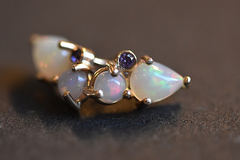 Puede incluir: Un anillo de oro con un grupo de tres &oacute;palos blancos con destellos iridiscentes y dos peque&ntilde;as piedras preciosas redondas de color violeta intenso. Las piedras est&aacute;n engastadas con garras, creando un dise&ntilde;o sobre una banda de oro pulido.