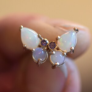Puede incluir: Un anillo con forma de mariposa que presenta dos &oacute;palos en talla pera para las alas superiores, dos &oacute;palos redondos en cabuj&oacute;n para las alas inferiores y dos peque&ntilde;as piedras redondas de color p&uacute;rpura en el centro, montados en metal.