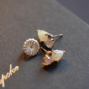 Puede incluir: Un par de pendientes de bot&oacute;n de plata con dos &oacute;palos en forma de l&aacute;grima y una peque&ntilde;a piedra preciosa morada en cada pieza. Los pendientes incluyen cierres met&aacute;licos circulares y texturizados. La palabra Bespoke se ve en letras doradas.