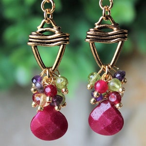 May include: Gold dangle earrings with a cluster of red, green, purple, and gold beads hanging from a gold wire frame.