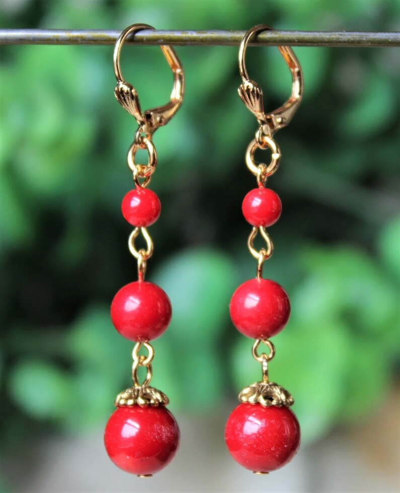 May include: A pair of long, dangling earrings with red beads and gold accents. The earrings have a simple, elegant design.