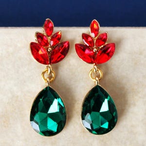May include: A pair of gold-tone drop earrings featuring a cluster of marquise-cut red crystals at the top, arranged in a leaf-like pattern, connected by a small gold ring to a large, faceted, pear-shaped emerald green crystal at the bottom.