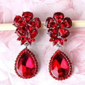 May include: A pair of red crystal teardrop earrings with a flower-shaped cluster of smaller crystals at the top.