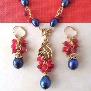 May include: A gold necklace and earrings set with dark blue pearls and red gemstone beads. The necklace features a gold pendant with a delicate design.