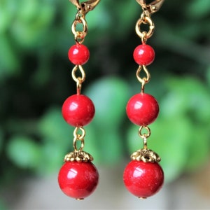 May include: A pair of red bead earrings with gold accents. The earrings are made with three round beads and a gold hook.