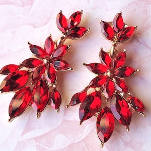Peut inclure: Une paire de boucles d'oreilles en cristal rouge avec un motif floral. Les boucles d'oreilles sont en métal doré et ont un design suspendu.