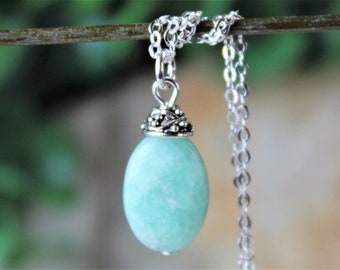 May include: A silver chain necklace with a light green oval pendant. The pendant has a silver filigree design around the top.