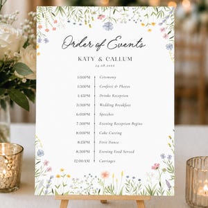 May include: A white wedding order of events sign featuring a delicate watercolor wildflower border in shades of pink, blue, yellow, and green. The text reads Order of Events, Katy & Callum, 24.08.202X, and lists a timeline from 1:00PM to 12:00AM.