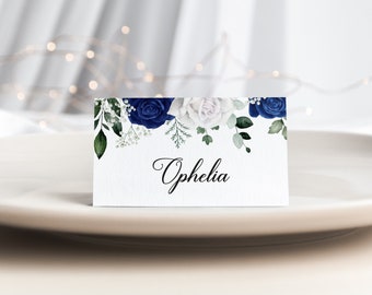 May include: White place card with blue and white floral design and the name "Ophelia" written in black cursive.