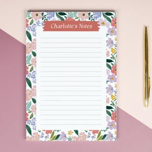 May include: A floral notepad with the text "Charlotte's Notes" in a red banner. The notepad is surrounded by a colorful floral border and a gold pen rests beside it. The notepad has lined pages.