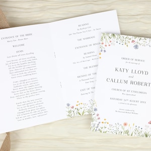 May include: A white wedding order of service programme featuring a floral border of small wildflowers in pink, blue, and yellow. The text includes the names Katy Lloyd and Callum Roberts, the date 24th August, and the full ceremony schedule inside.