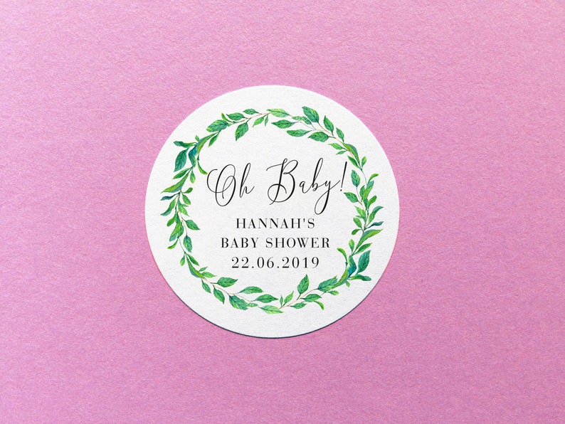Pu&ograve; includere: Etichetta rotonda bianca con un bordo di ghirlanda di foglie verdi. Il testo "Oh Baby!" &egrave; scritto in corsivo. Sotto il testo c'&egrave; "Hannah's Baby Shower 22.06.2019".