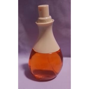 May include: A perfume bottle with a pear-shaped design. The bottle has a cream-coloured top and a clear body filled with orange-coloured liquid. The bottle is on a purple surface.
