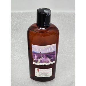 May include: A brown bottle of Goat Milk Aloe Shampoo with a black cap. The label features the words "Goat Milk Aloe Shampoo" over a lavender field image. The bottom label reads "Moonlit Flare Flower Goat Milk Shampoo".