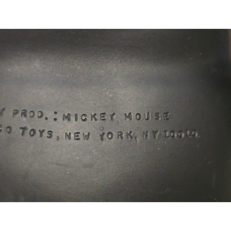May include: Close-up of a dark gray surface with embossed text. The text reads "PROD.: MICKEY MOUSE" and "GO TOYS, NEW YORK, NY 10019."