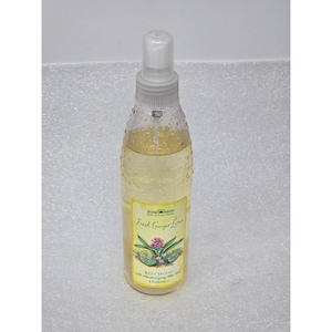 Puede incluir: Botella transparente de bruma corporal con un pulverizador blanco. La etiqueta dice "Fresh Ginger Lime" con ilustraciones de flores de jengibre y limas. La botella contiene un líquido amarillo claro y es de 236 ml.