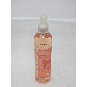 May include: A clear bottle of Plumeria body splash by Bath & Body Works. The bottle contains a light pink liquid and has a white spray nozzle. The label features a pink plumeria flower graphic and the text "Plumeria body splash" and "8 fl oz / 236 ml".