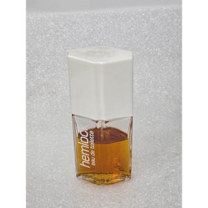 May include: A rectangular glass bottle of "hemlock eau de toilette" with a white cap. The bottle contains a golden-brown liquid. The text "hemlock" is printed vertically in a stylized font on the front of the bottle.