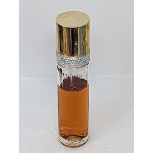 May include: A perfume bottle with a gold cap and a silver rhinestone band. The clear glass bottle contains a light brown liquid and has the words "Diamonds and Rubies" printed on it. The bottle is cylindrical and has a gold cap.