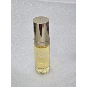 May include: A clear glass perfume bottle with a silver cap. The bottle contains a light yellow liquid and has the words "JOVAN MUSK" printed on the front. The bottle is cylindrical and appears to be a roll-on style.