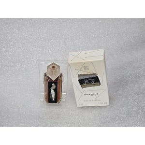 May include: A miniature Givenchy Hot Couture eau de parfum bottle with a clear geometric cap and a black label featuring a white silhouette design, accompanied by its white rectangular box printed with needle graphics and the text 5 ml .17 FL OZ.