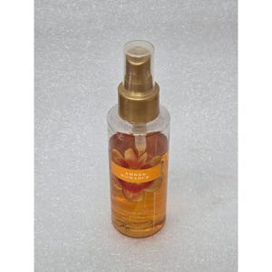 May include: A clear bottle of Amber Romance body mist with a gold-coloured pump and cap. The bottle contains a golden-coloured liquid and features a label with a floral design and the product name.