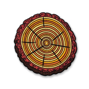 May include: A circular embroidered patch featuring a cross-section of a tree trunk. The design displays concentric rings in shades of yellow, orange, and red, with black radial lines and a dark brown textured border representing tree bark.