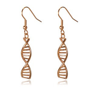 May include: A pair of rose gold-colored earrings. Each earring features a DNA double helix design, suspended from a simple hook. The earrings are displayed against a white background, with a slight reflection visible below.