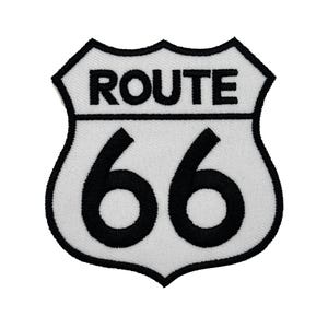 May include: A white Route 66 patch with black embroidered text and border. The words "ROUTE" are above the large black numbers "66" in a shield shape. This patch is likely for a jacket or bag.