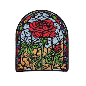 Könnte beinhalten: Gestickter Aufnäher mit einer roten Rose in einem Buntglasfenster-Design. Der Aufnäher hat einen schwarzen Rand und enthält grüne Blätter, eine Knospe und einen hellblauen Hintergrund. Das Design erinnert an ein klassisches Märchen.