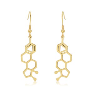 May include: A pair of gold-colored earrings in the shape of a molecular structure. The earrings have a hook closure and a series of connected hexagonal shapes. The design is symmetrical and hangs vertically.