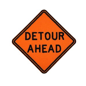 Könnte beinhalten: Oranges, rautenförmiges Patch mit schwarzem Rand. Die Worte „DETOUR AHEAD“ sind in fetten, schwarzen Großbuchstaben geschrieben. Geeignet zum Aufnähen oder Aufbügeln auf Textilien.