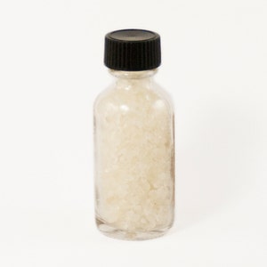 May include: A small glass bottle with a black lid filled with white crystals.