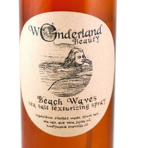 May include: A brown glass bottle with a label that says "Wonderland Beauty Beach Waves sea salt texturizing spray". The label also includes a drawing of a woman swimming in the ocean. The ingredients are listed on the label: distilled water, epsom salt, sea salt, aloe vera, jojoba oil, and honeysuckle essential oil.