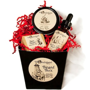 Puede incluir: Una caja de regalo negra con una etiqueta circular blanca que dice "Wonderland Beard Box" e incluye el texto "Incluye bálsamo para barba, aceite para barba, jabón para barba". La caja está llena de papel de seda rojo y contiene una barra de jabón marrón etiquetada "Beer Beard Shampoo Bar", una botella de vidrio transparente con un gotero etiquetada "Hemp & Jojoba Beard Oil", y un frasco blanco etiquetado "Sir Cedar Beard Balm".