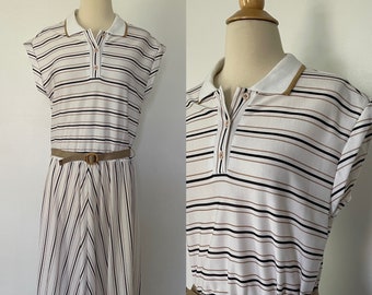 Puede incluir: Vestido polo blanco con rayas negras y beige. El vestido tiene cuello, mangas cortas y cinturón a juego. El vestido se exhibe en un maniquí.