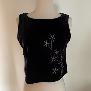 May include: A black velvet sleeveless top with a scoop neckline. The top has a floral design in a lighter colour on the front. The garment is displayed on a mannequin.