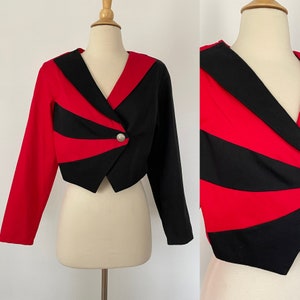Pode incluir: Um blazer curto em vermelho e preto. O casaco de mangas compridas apresenta um design de decote em V com fecho de botão prateado. O esquema de cores é uma combinação arrojada de riscas vermelhas e pretas.