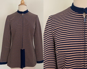 May include: A tan and navy blue striped jacket with a stand-up collar and a full-length zipper. The jacket has long sleeves and navy blue trim on the collar, cuffs, and bottom hem. The jacket is displayed on a mannequin.