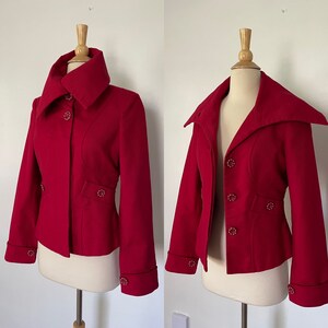 May include: A striking red jacket with a distinctive collar and decorative buttons. The jacket is displayed on a mannequin, highlighting its tailored fit and design. The sleeves have decorative buttons at the cuffs. The jacket's length is approximately 61 cm.