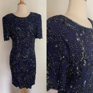 May include: Navy blue, short-sleeved dress with intricate sequin and bead embellishments. The dress features a round neckline and a fitted silhouette. The design includes floral and swirling patterns, creating a formal and elegant look.