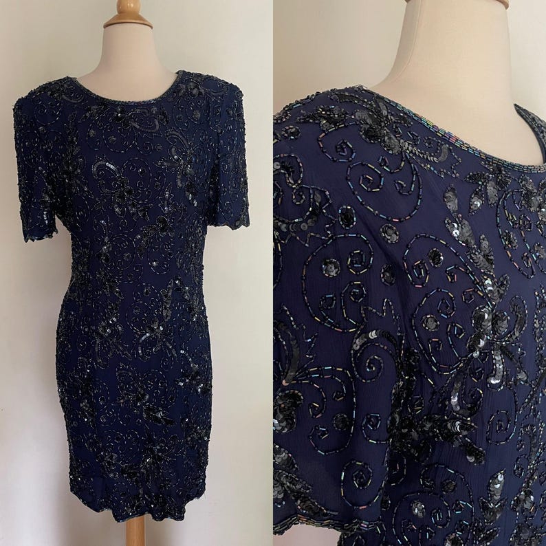 May include: Navy blue, short-sleeved dress with intricate sequin and bead embellishments. The dress features a round neckline and a fitted silhouette. The design includes floral and swirling patterns, creating a formal and elegant look.