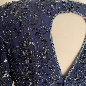 May include: Navy blue formal dress with intricate sequin and bead embellishments. The dress features a keyhole back and short sleeves. The design includes floral and swirling patterns, with iridescent accents around the neckline and keyhole.