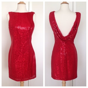 May include: A dazzling red sequin dress displayed on a mannequin. The sleeveless dress features a scoop neckline and a fitted silhouette. The back of the dress has a cowl neck design. The dress is a vibrant red color, perfect for a special occasion.
